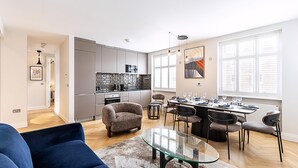 A modern living room with a glass coffee table, a blue sofa, and a dining area with a table set for four. - Elegant Marylebone/baker St Escape (London)