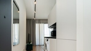 A modern kitchen with a washing machine, a dining area with a table and chairs, and a large window with curtains. - New central studio with balcony (Limassol)