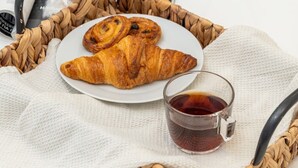 A tray with croissants and a cup of tea, placed on a white table with a magazine and a woven basket. - New central studio with balcony (Limassol)