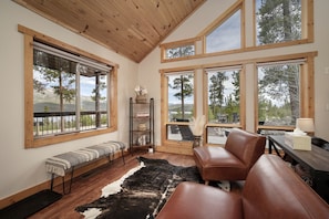 A room with a wooden ceiling, large windows, a bench, a leather couch, a rug, and a bookshelf. - Exceptional Luxury Cabin with Hot Tub, Games Room, and Fire Pit with Rocky Mountain Views in Grand Lake, Colorado (Grand Lake)
