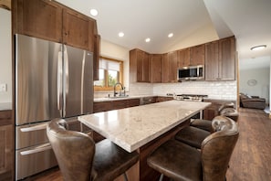 A modern kitchen with a large island, stainless steel appliances, wooden cabinets, and leather bar stools. - Exceptional Luxury Cabin with Hot Tub, Games Room, and Fire Pit with Rocky Mountain Views in Grand Lake, Colorado (Grand Lake)