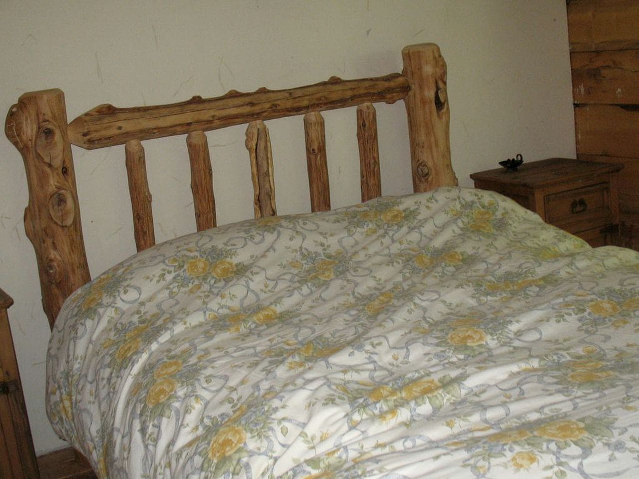 A wooden bed with a floral bedspread in a room with wooden furniture and a plain wall.