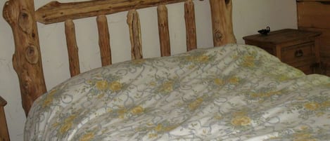 A wooden bed with a floral bedspread in a room with wooden furniture and a plain wall.