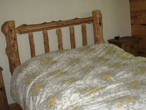 Een houten bed met een bloemenlaken in een kamer met houten meubels en een effen muur.