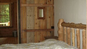 A wooden cabin bedroom with a bed, a window, and a door.