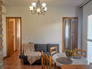A cozy living room with a sofa, a dining table with placemats, a chandelier, and wooden doors. - Las Rosas 6 by Casasol (Frigiliana)