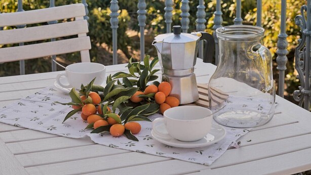Een tafel gedekt met een koffiepot, kop en karaf op een balkon met uitzicht op een wijngaard.