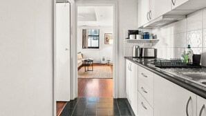 A modern kitchen with white cabinets, a black countertop, and a stainless steel kettle. - Cute & Cosy - Walk to Sydney CBD & Harbour (Woolloomooloo)