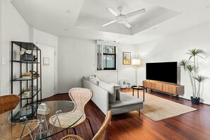 A modern living room with a sofa, television, and a dining area with chairs and a glass table. - Cute & Cosy - Walk to Sydney CBD & Harbour (Woolloomooloo)