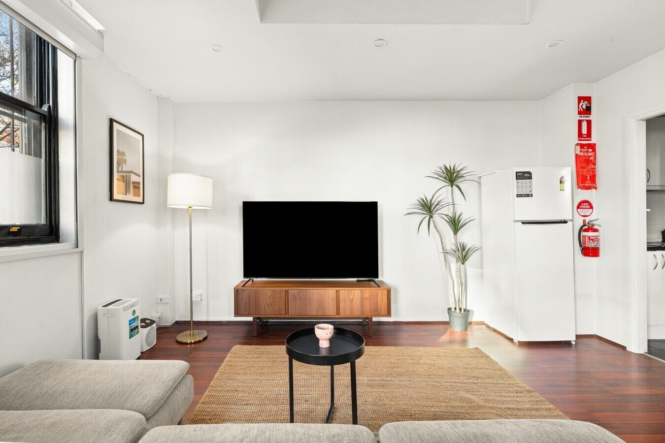 Una sala de estar moderna con un televisor de pantalla plana, un mueble de madera, un sofá, una mesa de centro, una lámpara de pie y una planta en maceta.