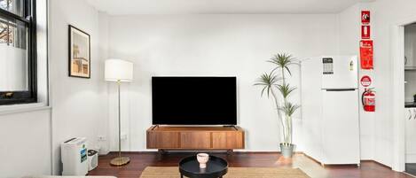 Una sala de estar moderna con un televisor de pantalla plana, un mueble de madera, un sofá, una mesa de centro, una lámpara de pie y una planta en maceta.