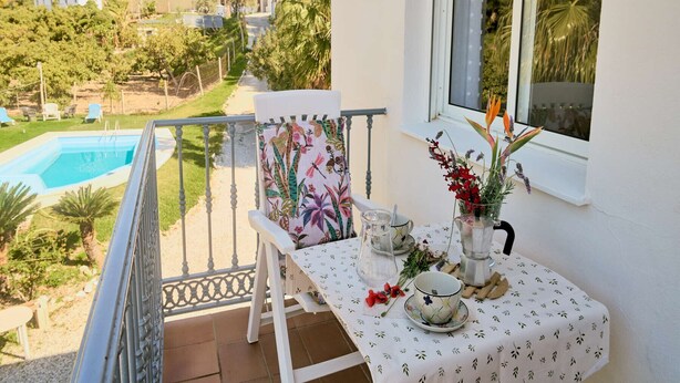 Un balcón con una mesa dispuesta para tomar té, vista a una piscina y un edificio al fondo.