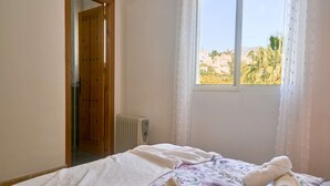 Un dormitorio con cama, ventana con vistas, radiador y puerta de madera.