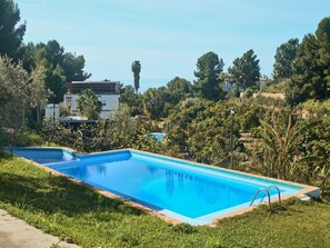 Ein rechteckiger Swimmingpool mit klarem, blauem Wasser, umgeben von Gras und Bäumen, mit Gebäuden im Hintergrund.