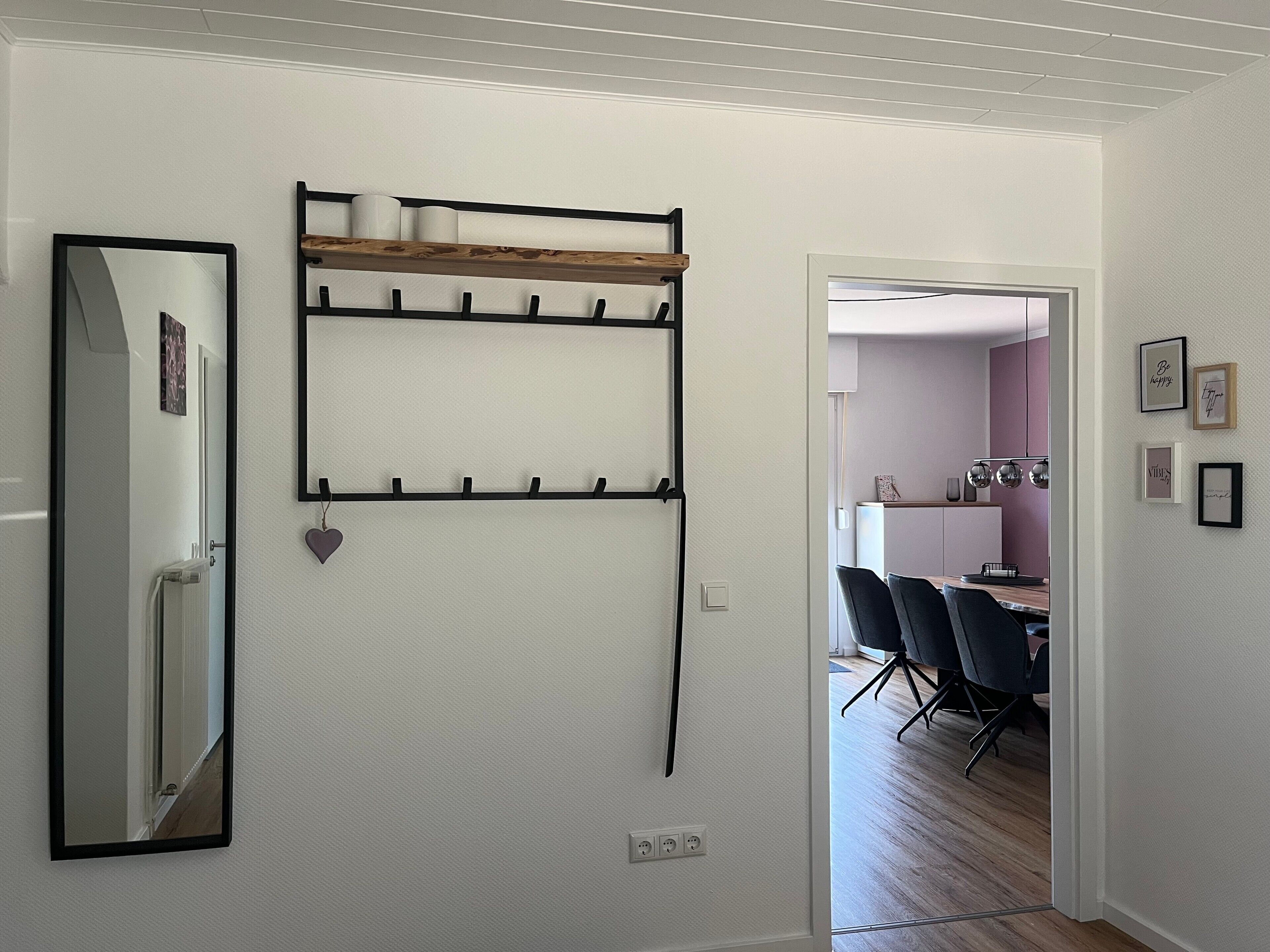Una habitación con un espejo, un estante con ganchos y una puerta que da a otra estancia.
