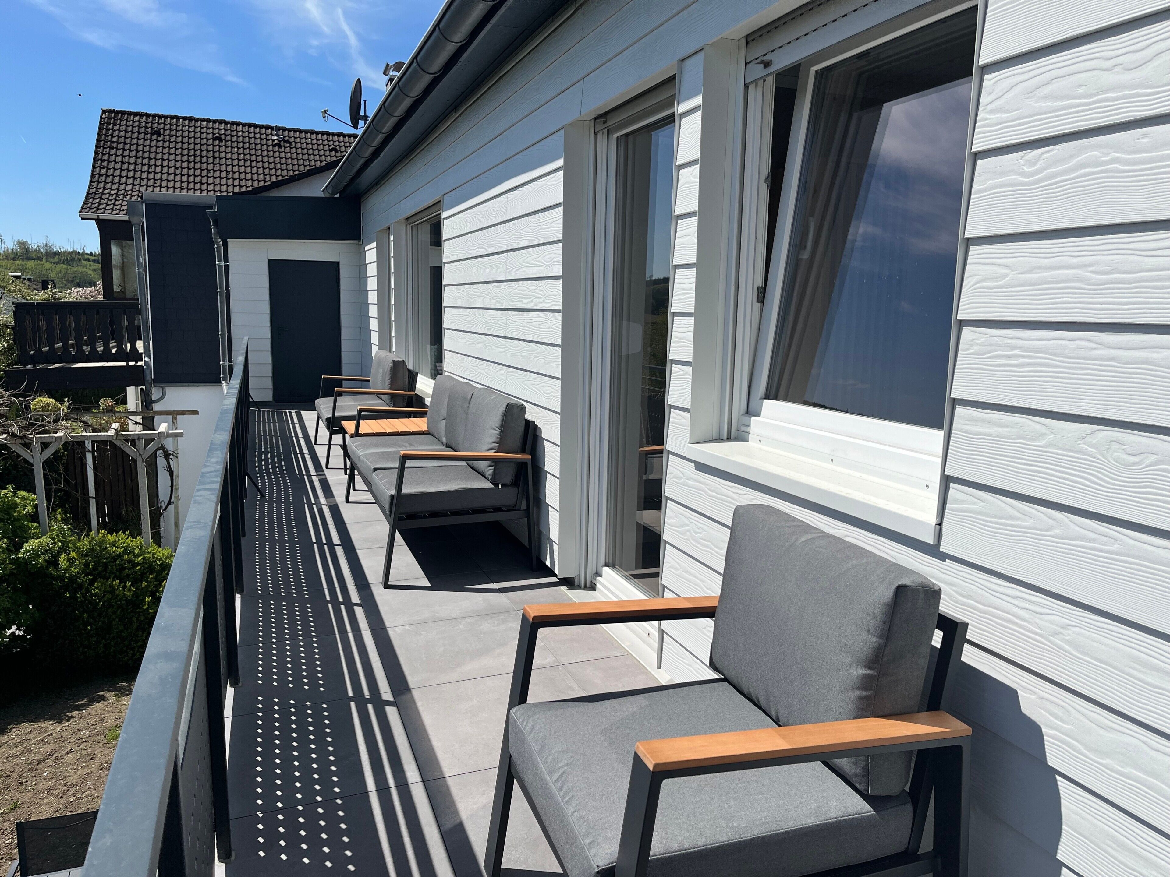 En balkon med udendørs møbler, en parabolantenne og et hus med hvidt facadebræt.