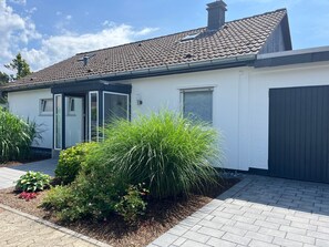 Una casa moderna con techo de tejas, garaje y jardín con diversas plantas.