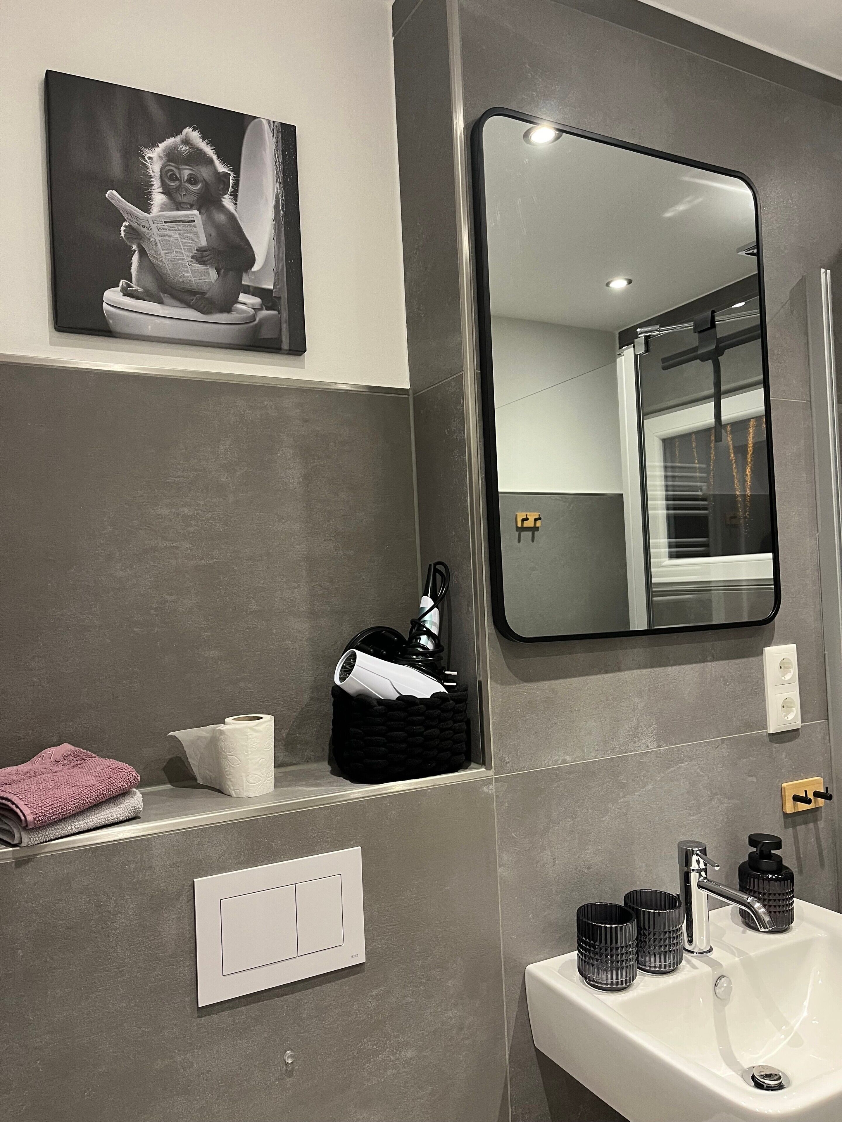 Une salle de bain avec un grand miroir, un lavabo, un porte-serviettes, un luminaire fixé au mur et un tableau encadré.