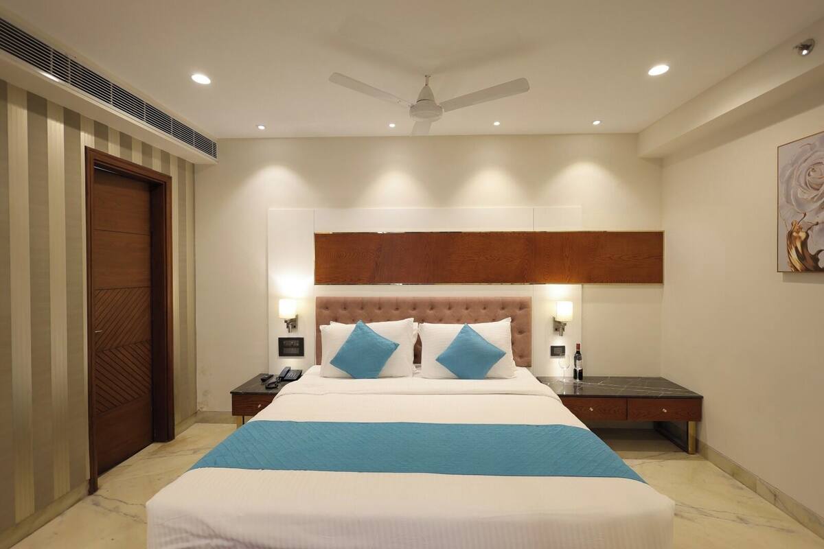Ein Hotelzimmer mit einem großen Bett, zwei Nachttischen, einem Deckenventilator und einem an der Wand hängenden Kunstwerk.
