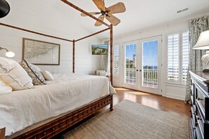 A bedroom with a four-poster bed, a ceiling fan, a large window with a view, and a door leading to a balcony.