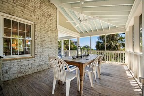 A covered patio with a wooden table and white chairs, a brick wall, and a view of the ocean.