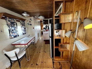 A kitchen with wooden cabinets, a stove, and a dining area with a table and chairs. - Retro Trailer Rental for Glamping Getaway in Joshua Tree, California (Joshua Tree)