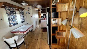 A kitchen with wooden cabinets, a stove, and a dining area with a table and chairs. - Retro Trailer Rental for Glamping Getaway in Joshua Tree, California (Joshua Tree)