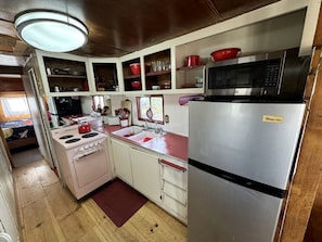 A compact kitchen with a stove, sink, and refrigerator, featuring wooden cabinets and a microwave. - Retro Trailer Rental for Glamping Getaway in Joshua Tree, California (Joshua Tree)