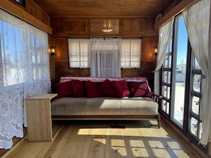 A cozy cabin-style room with a bed, a small wooden table, and large windows. - Retro Trailer Rental for Glamping Getaway in Joshua Tree, California (Joshua Tree)