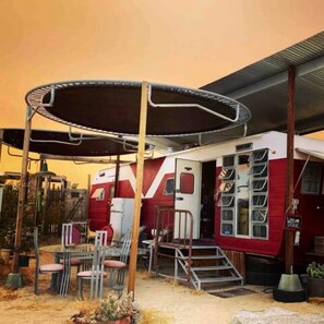 A red RV with a covered porch, outdoor seating, and a staircase leading to the entrance. - Retro Trailer Rental for Glamping Getaway in Joshua Tree, California (Joshua Tree)
