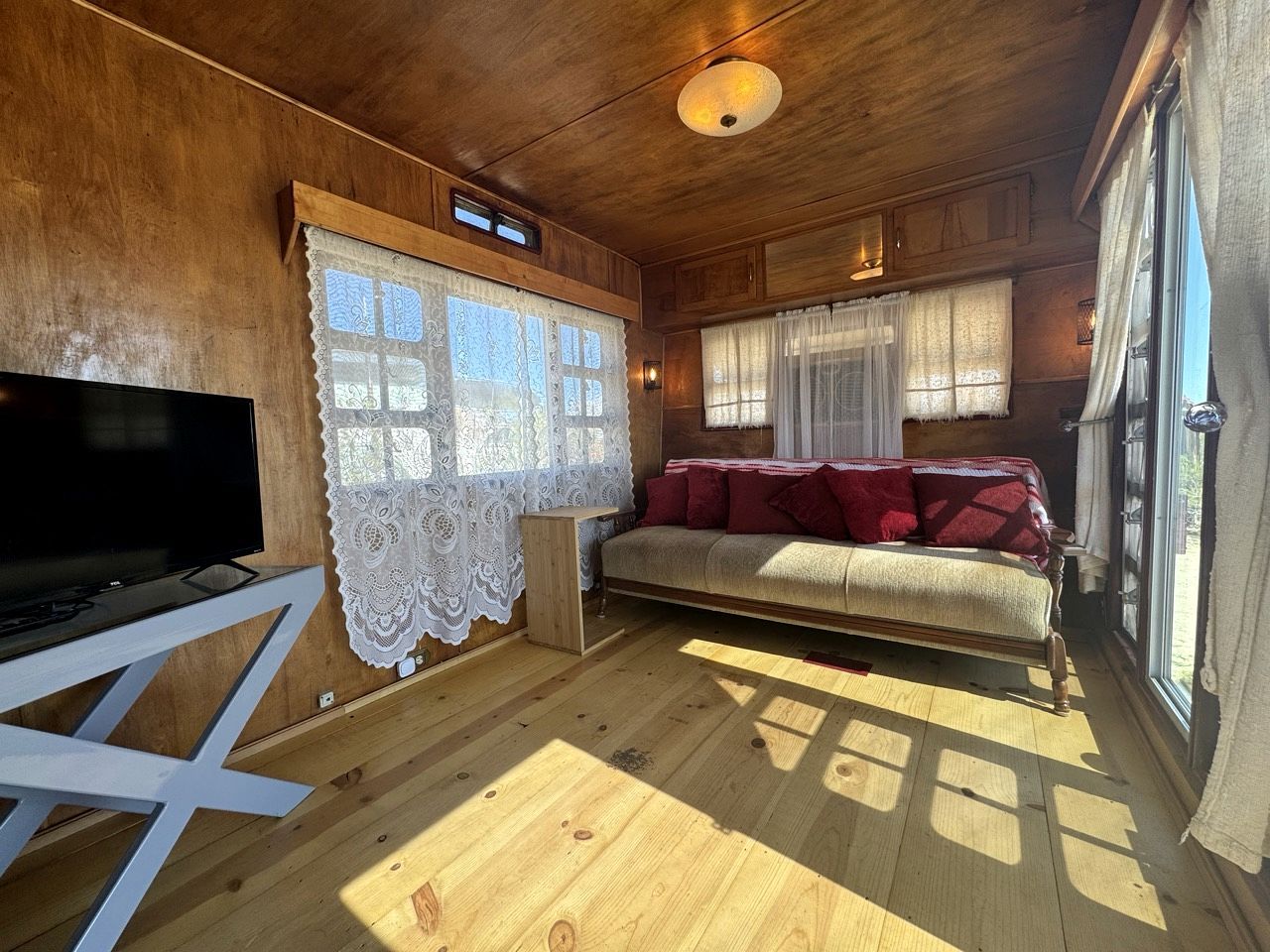A wooden interior with a sofa, TV, and lace curtains.