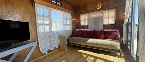 A wooden interior with a sofa, TV, and lace curtains.