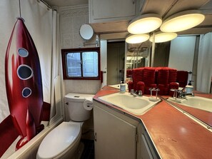 A compact bathroom with a toilet, two sinks, a mirror, and a red towel rack. - Retro Trailer Rental for Glamping Getaway in Joshua Tree, California (Joshua Tree)