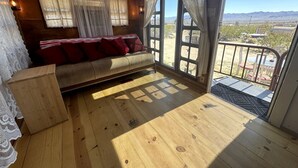 A wooden-floored room with a sofa and curtains, a view of the outdoors, and a door leading outside. - Retro Trailer Rental for Glamping Getaway in Joshua Tree, California (Joshua Tree)