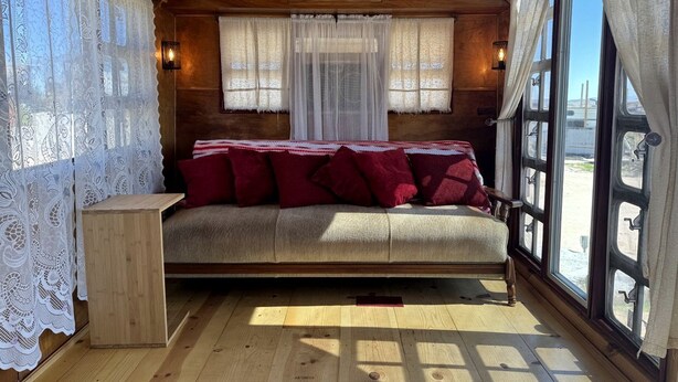 A cozy cabin-style room with a bed, a small wooden table, and large windows. - Retro Trailer Rental for Glamping Getaway in Joshua Tree, California (Joshua Tree)
