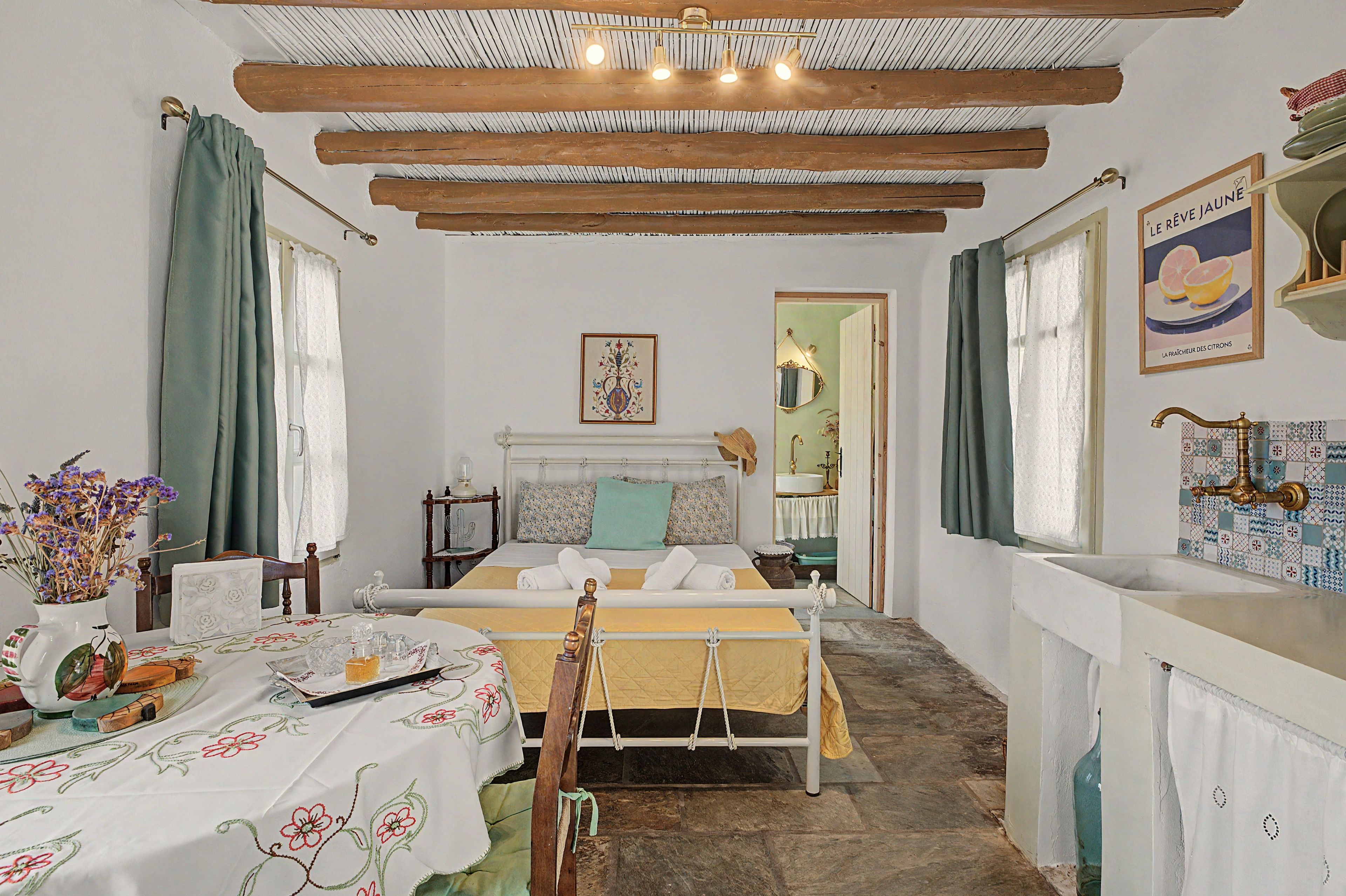 Una habitación con una cama, una mesa con un florero y una ventana con cortinas.