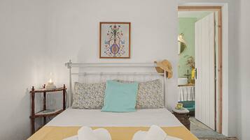 Una cama bien hecha con edredón blanco y dos toallas blancas, una mesita de noche con lámpara, y una obra de arte enmarcada sobre la cama.