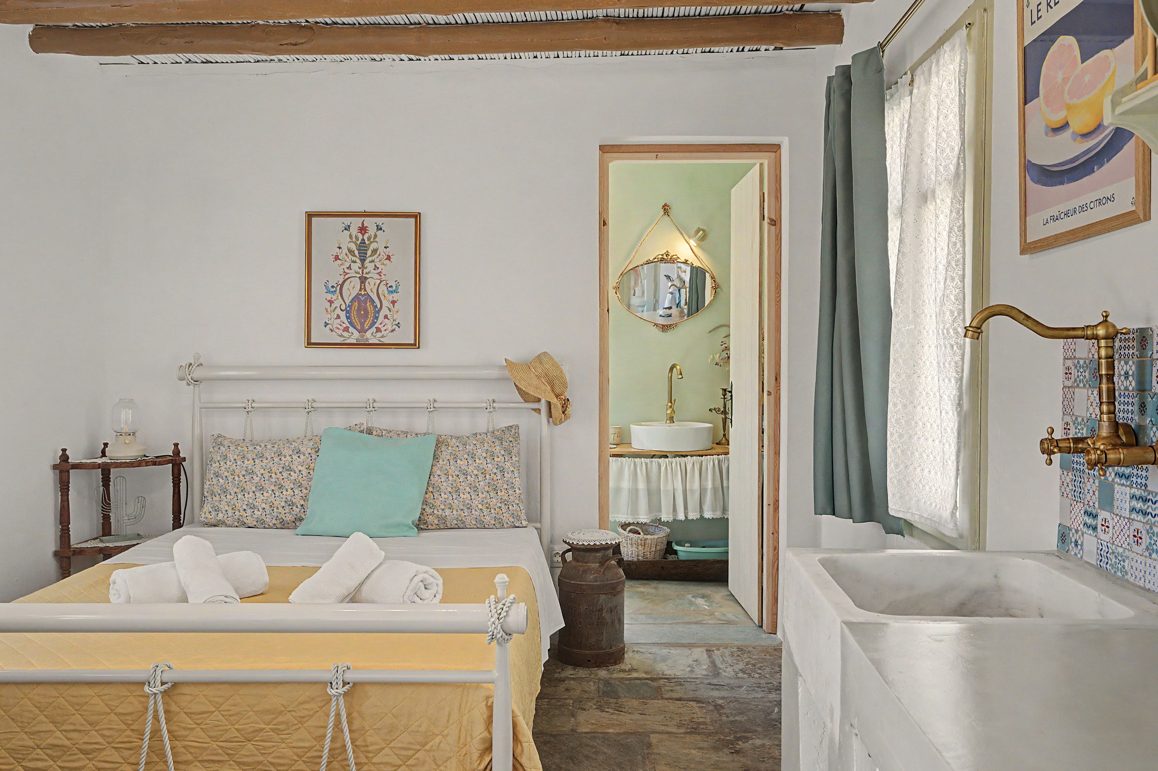 A bedroom with a bed, a bedside table, a mirror, a sink, and a bathtub.