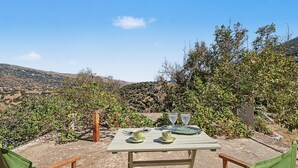 Un espace de restauration en plein air avec une table dressée pour deux personnes, entouré de verdure et avec des collines en arrière-plan.