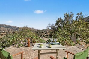 An outdoor dining area with a table set for two, surrounded by greenery and hills in the background. - Oak Farm Guesthouse Junior (Andros)