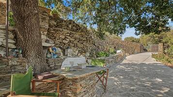 A rustic outdoor seating area with stone walls, a wooden table, and a chair.