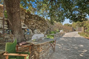 A rustic outdoor seating area with stone walls, a wooden table, and a chair. - Oak Farm Guesthouse Junior (Andros)