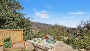 Une table offrant une vue sur un paysage vallonné, avec une clôture en bambou et des chaises vertes.