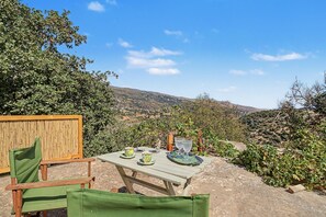 A table with a view of a hilly landscape, a bamboo fence, and green chairs. - Oak Farm Guesthouse Junior (Andros)
