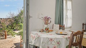 Un coin repas avec une table dressée pour deux personnes, un vase rempli de fleurs et une vue sur l’extérieur.