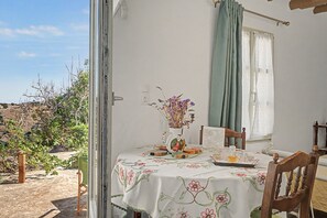 A dining area with a table set for two, a vase with flowers, and a view of the outdoors. - Oak Farm Guesthouse Junior (Andros)