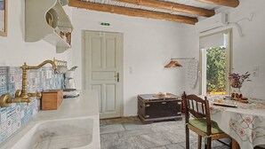 Cocina rústica con un lavabo, vigas de madera, una puerta blanca y una ventana con vistas a la vegetación.