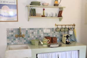 Una cocina con salpicadero de azulejos, un lavabo, un hervidor, una cafetera y diversos utensilios de cocina.