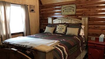 A wooden cabin-style room with a bed, a nightstand, and a window with curtains.