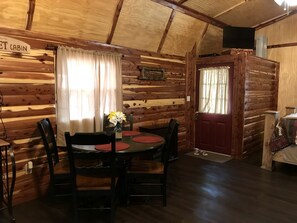 A log cabin interior with a dining table, chairs, a television, and a bed.